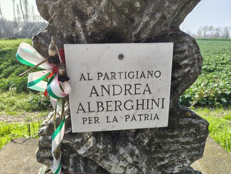 Cippo commemorativo dedicato al partigiano Andrea Alberghini, immerso in un campo verde.