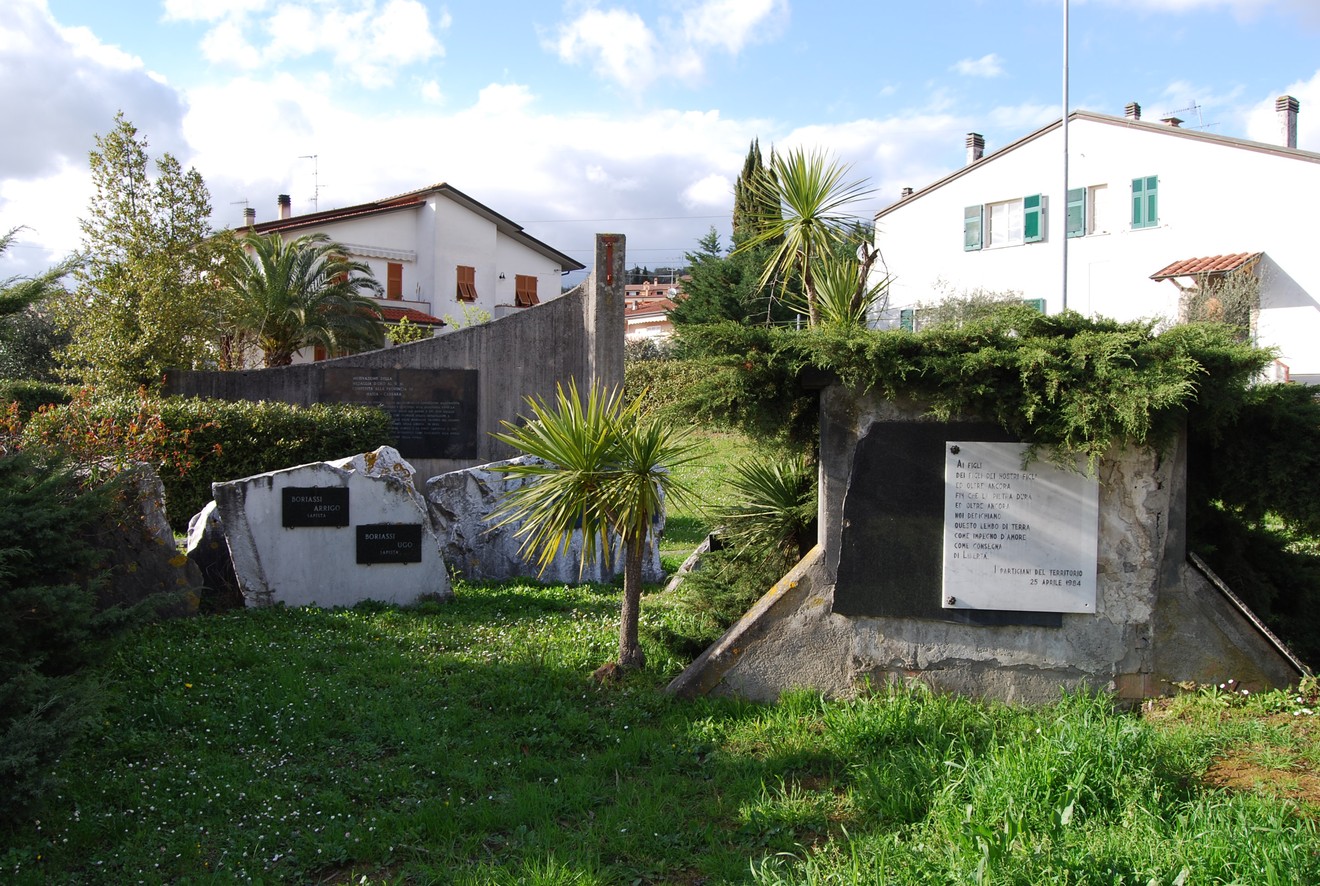 Monumento nel Parco della Resistenza di Caniparola, circondato da verde e edifici, dedicato alla memoria storica.