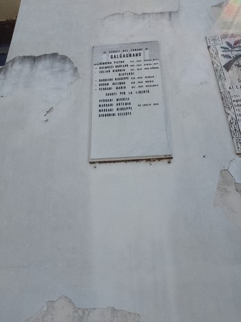 Lapide commemorativa su una parete, dedicata ai caduti in guerra, con nomi incisi e segni del tempo.