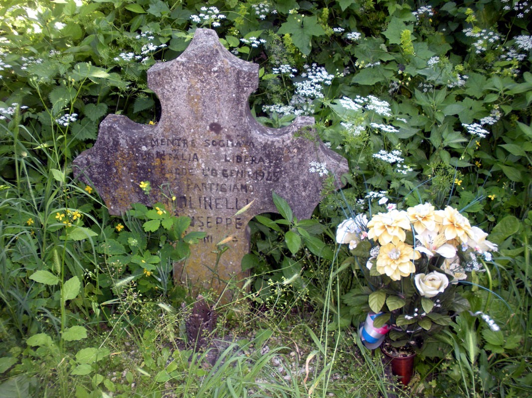 Croce dedicata a Molinelli, in memoria di un partigiano, circondata da natura e fiori.