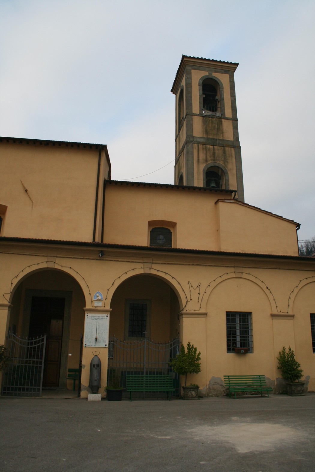 Lapide commemorativa e facciata della chiesa di Piteccio, con campanile sullo sfondo.