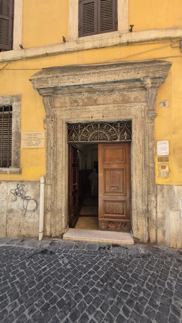 Ingresso di un edificio con una lapide commemorativa, decorato da una cornice in pietra e pareti gialle.