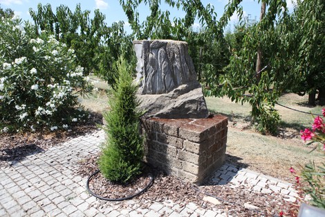 Monumento ai Caduti della Libertà circondato da un giardino, con rilievi sulle pareti e vegetazione verde.