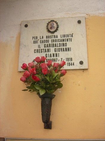 Lapide dedicata a Giovanni Crestani, garibaldino caduto per la libertà, con fiori rossi ornamentali.