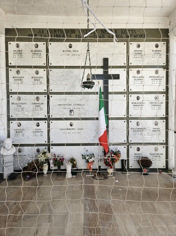 Sacrario dei Partigiani con pietre commemorative, una croce nera e decorazioni floreali, simbolo di memoria e resistenza.