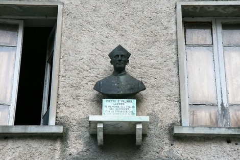 Busto di Don Lazzeri con lapide commemorativa su facciata di un edificio, in un contesto storico.