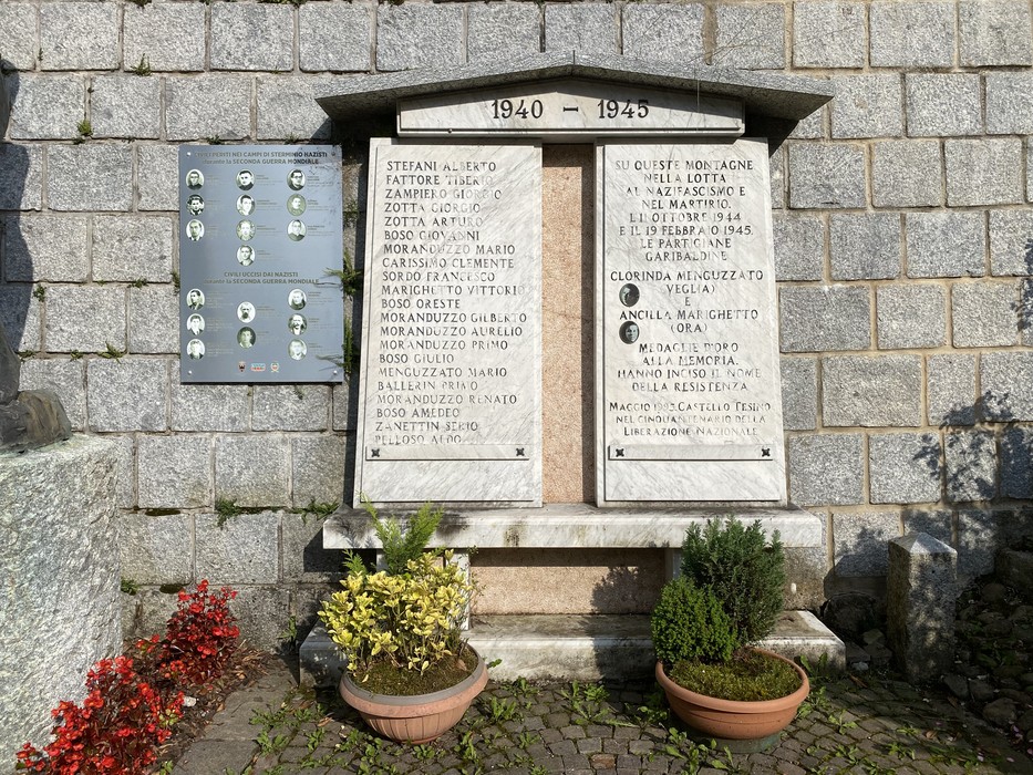 Monumento ai caduti di Castello Tesino, con iscrizioni commemorative su pietra e decorazioni floreali.