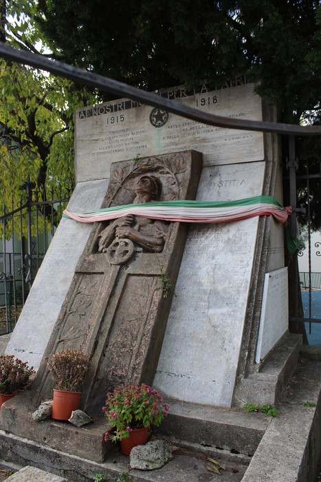 Monumento decorato con epigrafi in ricordo dei caduti, con piante e drappi tricolore.