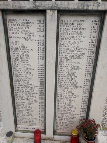 Monumento commemorativo con nomi incisi dei caduti per la libertà, circondato da fiori e candele.