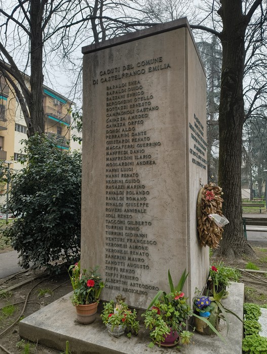Monumento ai partigiani a San Ruffillo, con nomi incisi e adornato di fiori e una corona commemorativa.