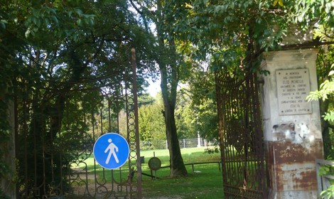 Ingresso del parco con chiusura in ferro e segnale di attraversamento pedonale su sfondo verde di natura.