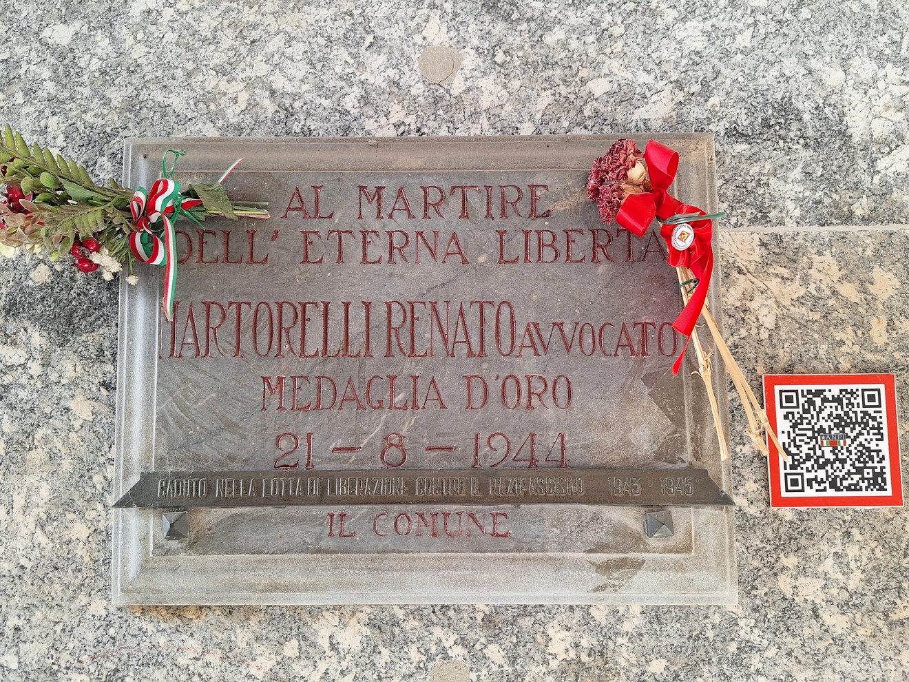 Lapide commemorativa dedicata a Renato Martorelli, con decorazioni floreali e simboli celebrativi.