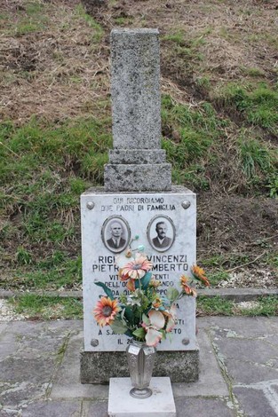 Cippo commemorativo con immagini e fiori, in memoria di Righi e Vincenzi, situato in un luogo di ricordo.