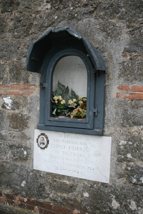 Lapide commemorativa a Chisci, partigiano di Belfego, con fiori celebrativi e dedica in memoria.