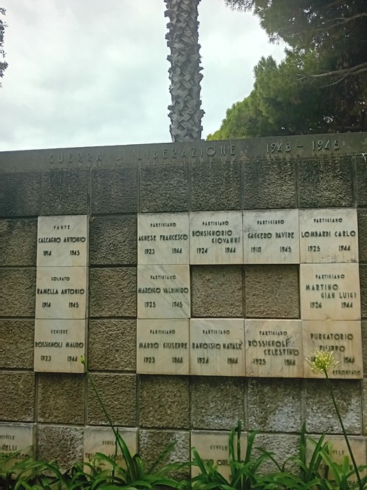 Monumento ai caduti con iscrizioni commemorative e decorazioni floreali, simbolo di memoria storica.