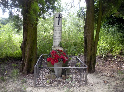 Cippo commemorativo con fiori rossi, circondato da alberi in un'area verde, simbolo di memoria e rispetto.