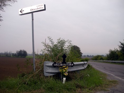 Croce commemorativa a Collarini, con fiori, posta vicino a una strada di campagna.