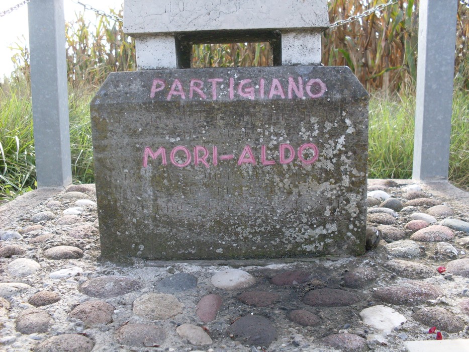Cippo commemorativo dedicato al partigiano Aldo Mori, situato in un contesto naturale.