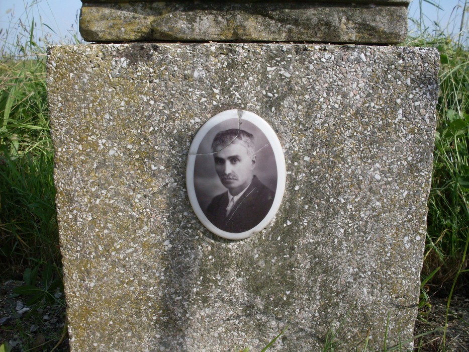 Cippo commemorativo con una fotografia incastonata, immerso nel verde. Rappresenta la memoria di una persona.