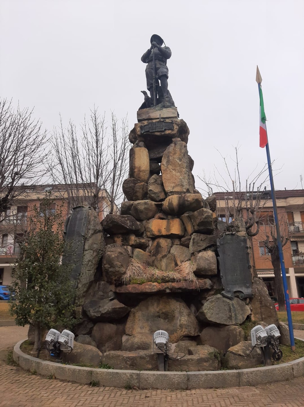 Monumento ai caduti con una statua centrale su un basamento di rocce e vegetazione circostante.