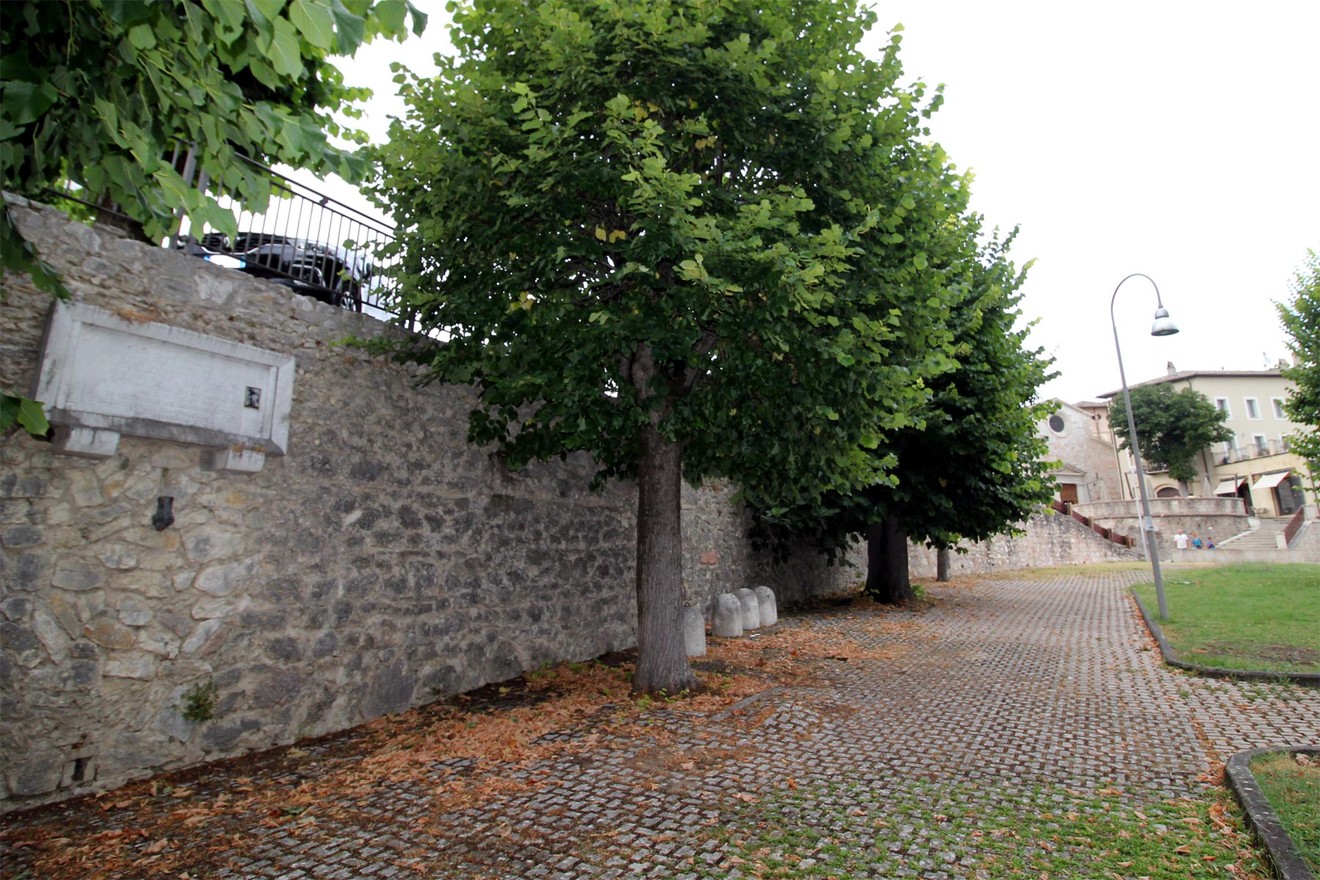 Lapide commemorativa ad Allegretti, incastonata in un muro di pietra, circondata da alberi.