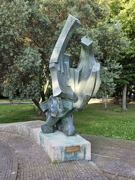 Scultura astratta del "Monumento alla Resistenza" immersa nel verde, simbolo di commemorazione storica.
