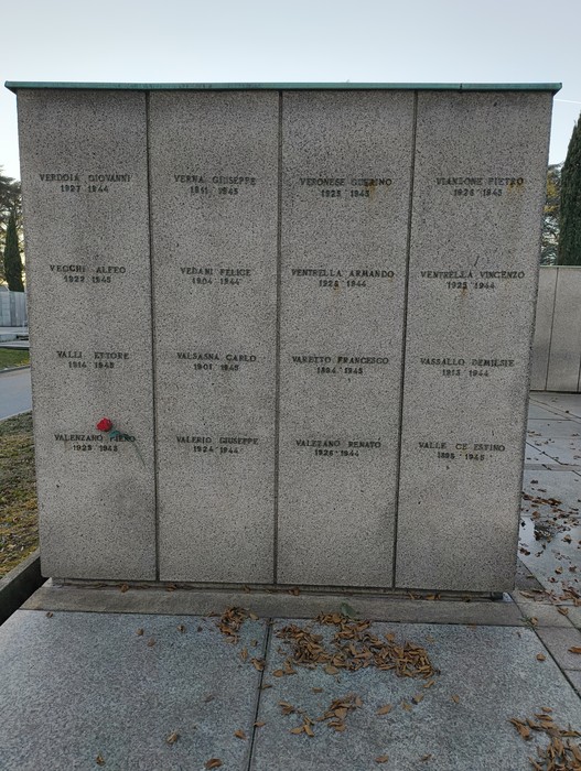 Monumento commemorativo in pietra con nomi di caduti, circondato da foglie secche. Atmosfera di rispetto e memoria.