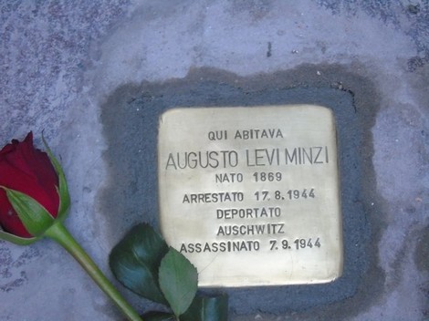Pietra d'inciampo dedicata a Augusto Levi Minzi, con rosa rossa accanto, commemorando la sua tragica storia.