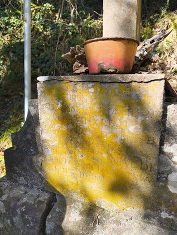 Monumento a Naldi, con una base stone e un vaso in terracotta, immerso nella natura.