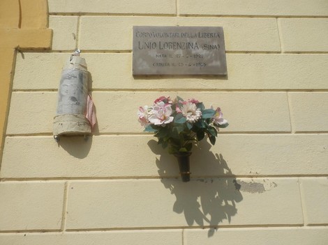 Lapide commemorativa dedicata a Unio Lorenzi, con decorazioni floreali e simbolo della libertà.