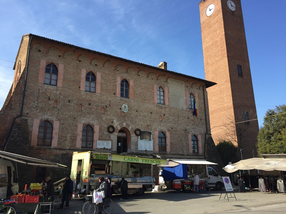 Lapide ai caduti di Villanterio, memoriale storica in un contesto di mercato con torre orologio.