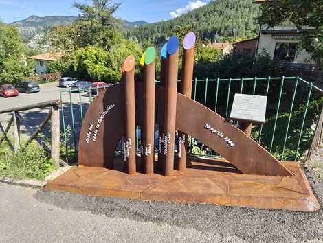 Monumento commemorativo per le vittime della strage di Castagno, con colonne colorate su base scultorea.