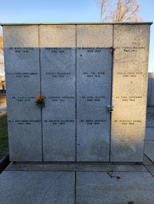 Monumento commemorativo al "Campo della Gloria" con nomi incisi e un omaggio floreale.
