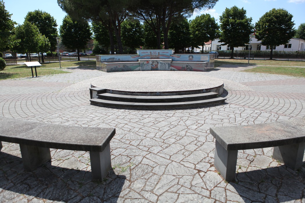 Murali colorati nel parco della Liberazione, con panchine in un'area centrale circondata da alberi.