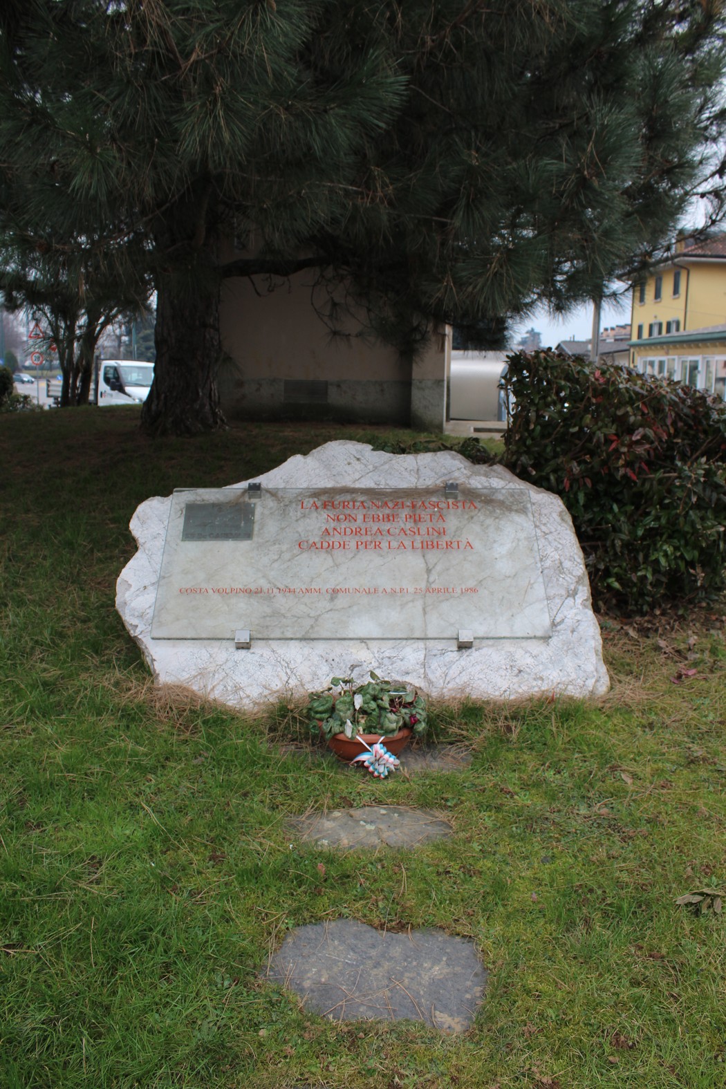 Monumento a Caslini, con una base in pietra e fiori, circondato da un'area verde.