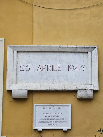 Lapide commemorativa che celebra il 25 aprile 1945, data della Liberazione, su sfondo giallo.