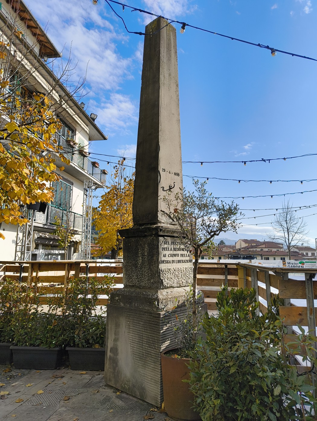 Obelisco del Decennale, monumento commemorativo situato in un contesto urbano con vegetazione e cielo azzurro.