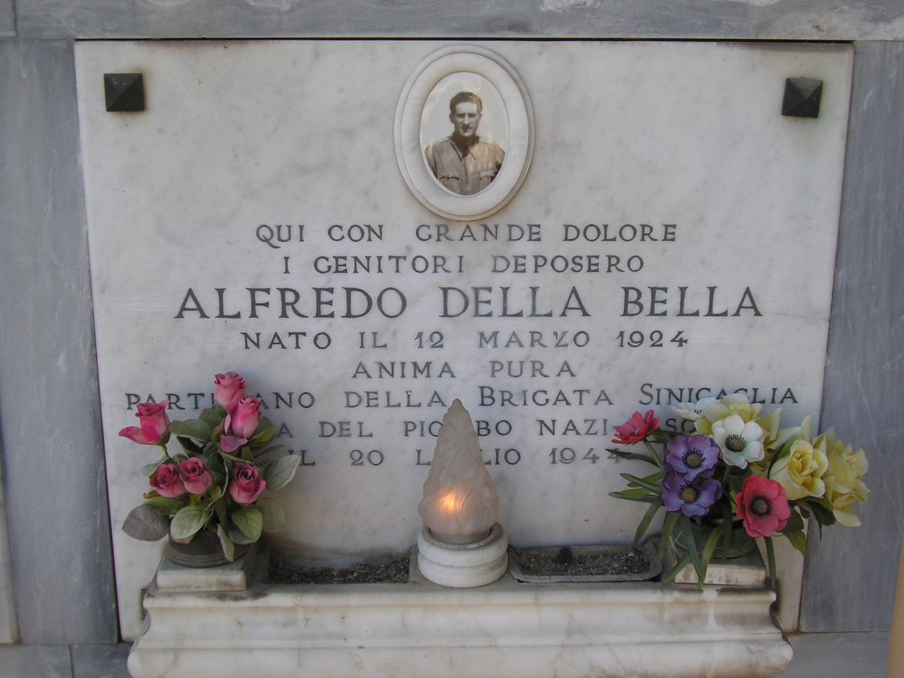 Sepolcro di Alfredo Della Bella, decorato con fiori e una foto, in onore di un partigiano.