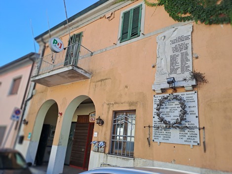 Lapide commemorativa ai Caduti di Gello affissa su un edificio, con dettagli architettonici circostanti.