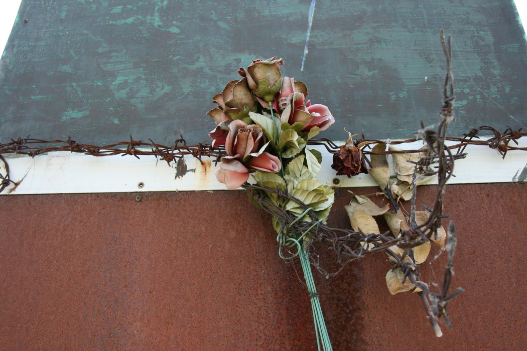 Monumento ai caduti nei lager, con fiori di commemorazione e filo spinato in segno di memoria.