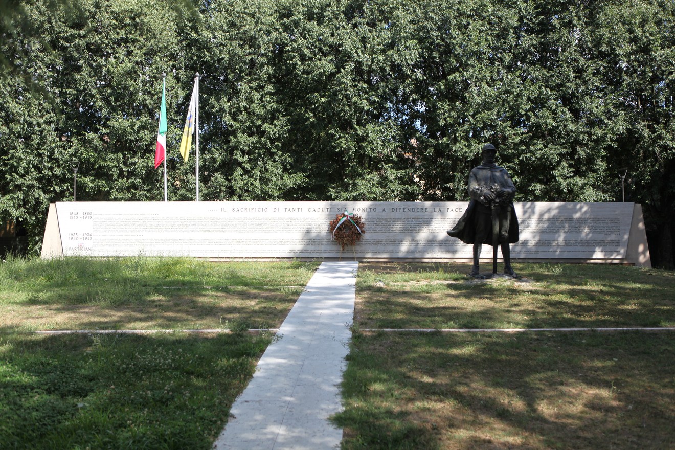 Monumento ai Caduti con una statua e una lastra commemorativa circondata da alberi.