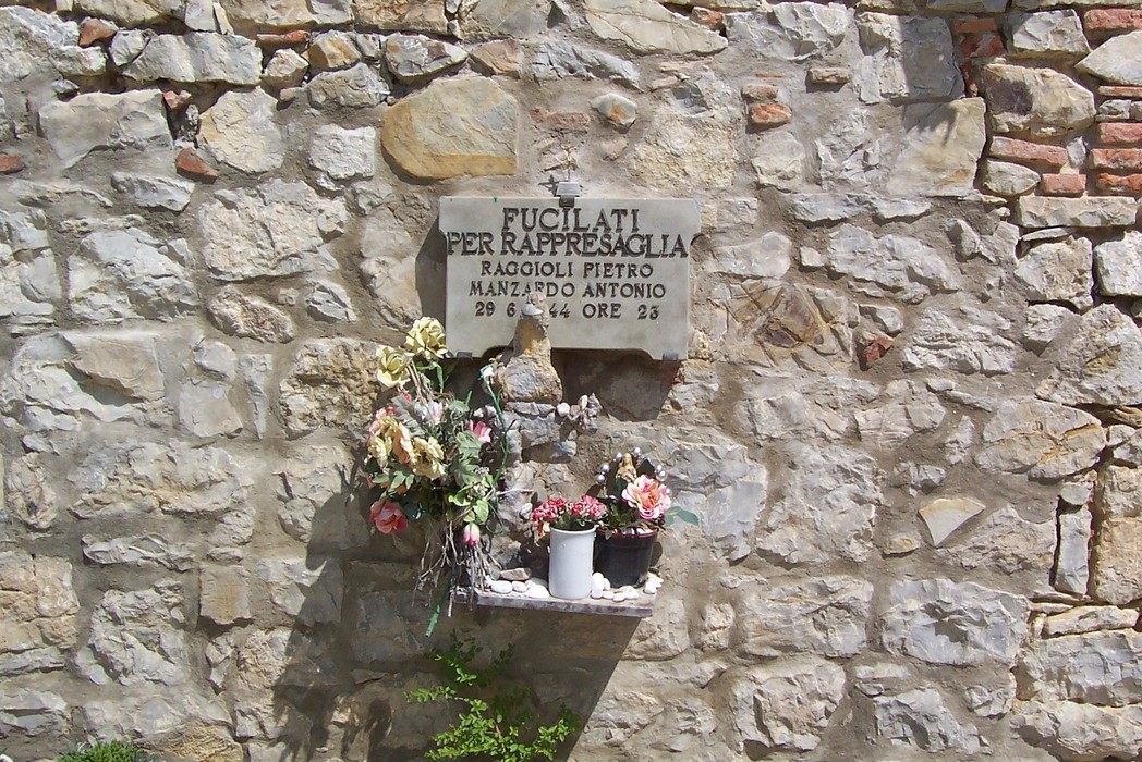 Lapide commemorativa dedicata a Raggioli e Manzardo, con fiori e messaggi di ricordo sulla parete di pietra.