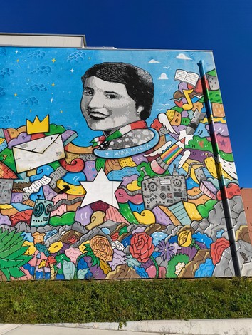 Murale colorato che celebra figure storiche, con elementi astratti e floreali, sul muro di Enriques Agnoletti.