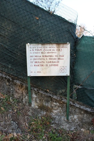 Lapide commemorativa dedicata alla famiglia Volpi, situata in un'area naturale con rete di protezione.