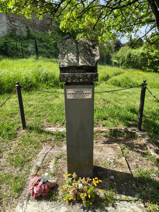 Cippo commemorativo a Meuret, circondato da vegetazione e fiori, in un'area verde e tranquilla.