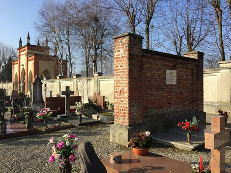 Lapide commemorativa nel cimitero con fiori e monumenti in un ambiente tranquillo e sereno.