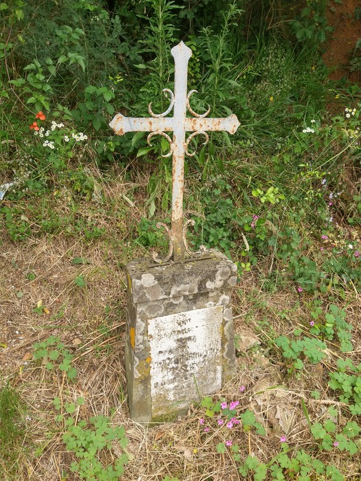 Monumento commemorativo con croce metallica in un contesto naturale, circondato da vegetazione.