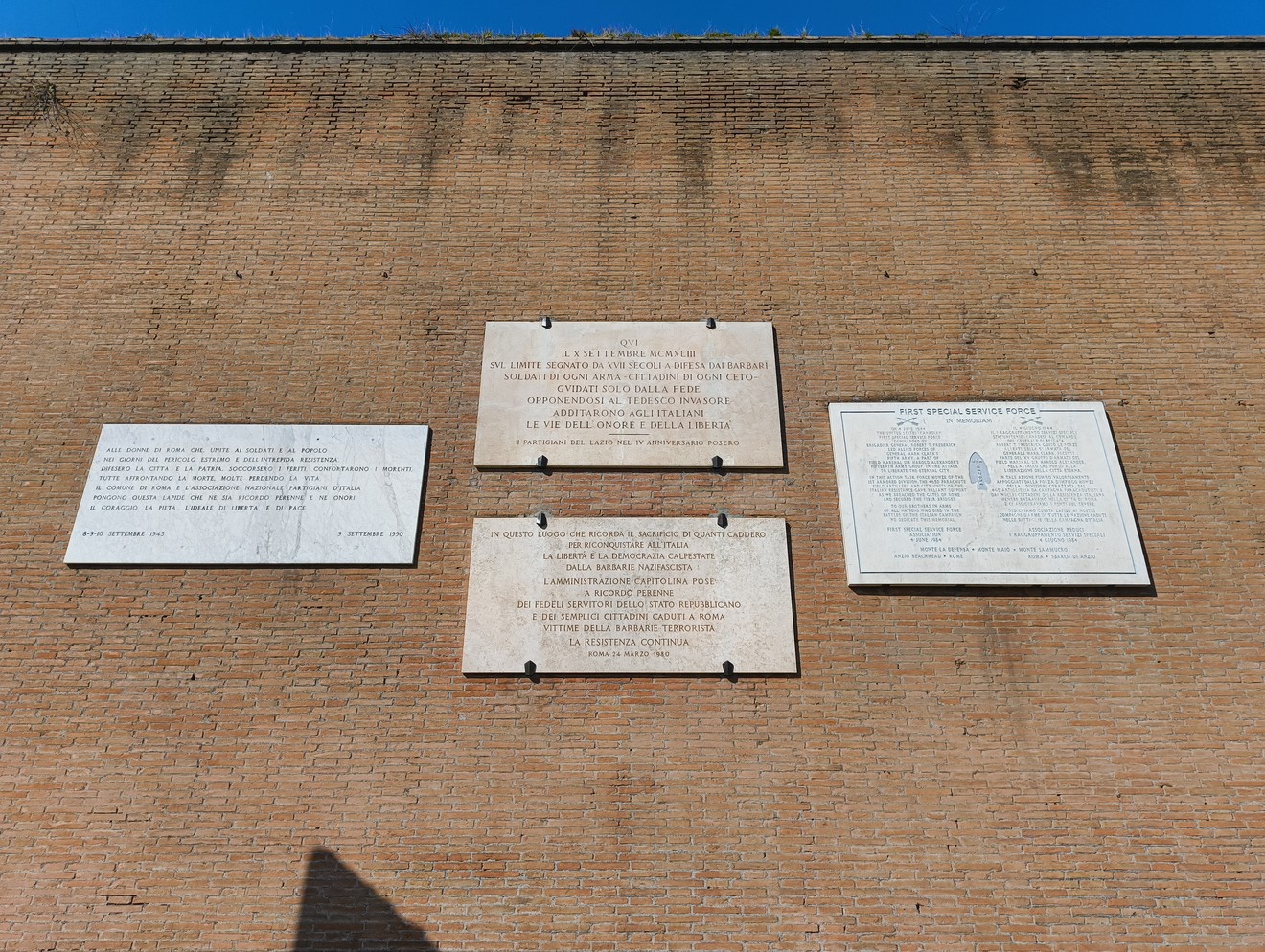 Lapidi storiche su una parete di mattoni a Porta San Paolo, con testo commemorativo e di riflessione.