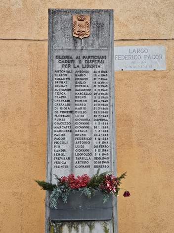 Monumento commemorativo ai caduti per la libertà, con iscrizioni e decorazioni floreali.