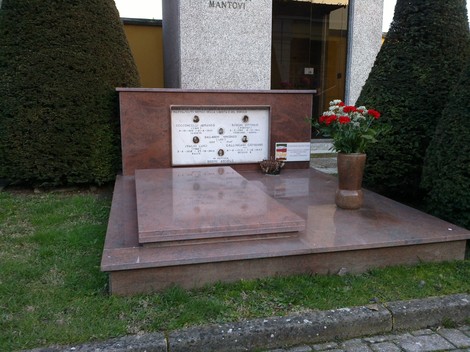Monumento commemorativo ai caduti di Pratofontana, con fiori e lapide in marmo su base verde.